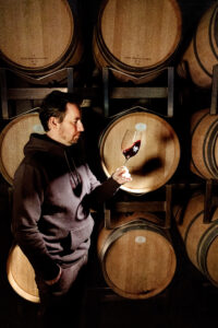 Patrick Bayer im Weinkeller mit einem Glas des alkoholfreien Rotweins Zeronimo Leonis Blend in der Hand 